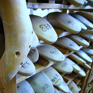Cheese wheels stacked on wooden shelves, labeled with brown ink.