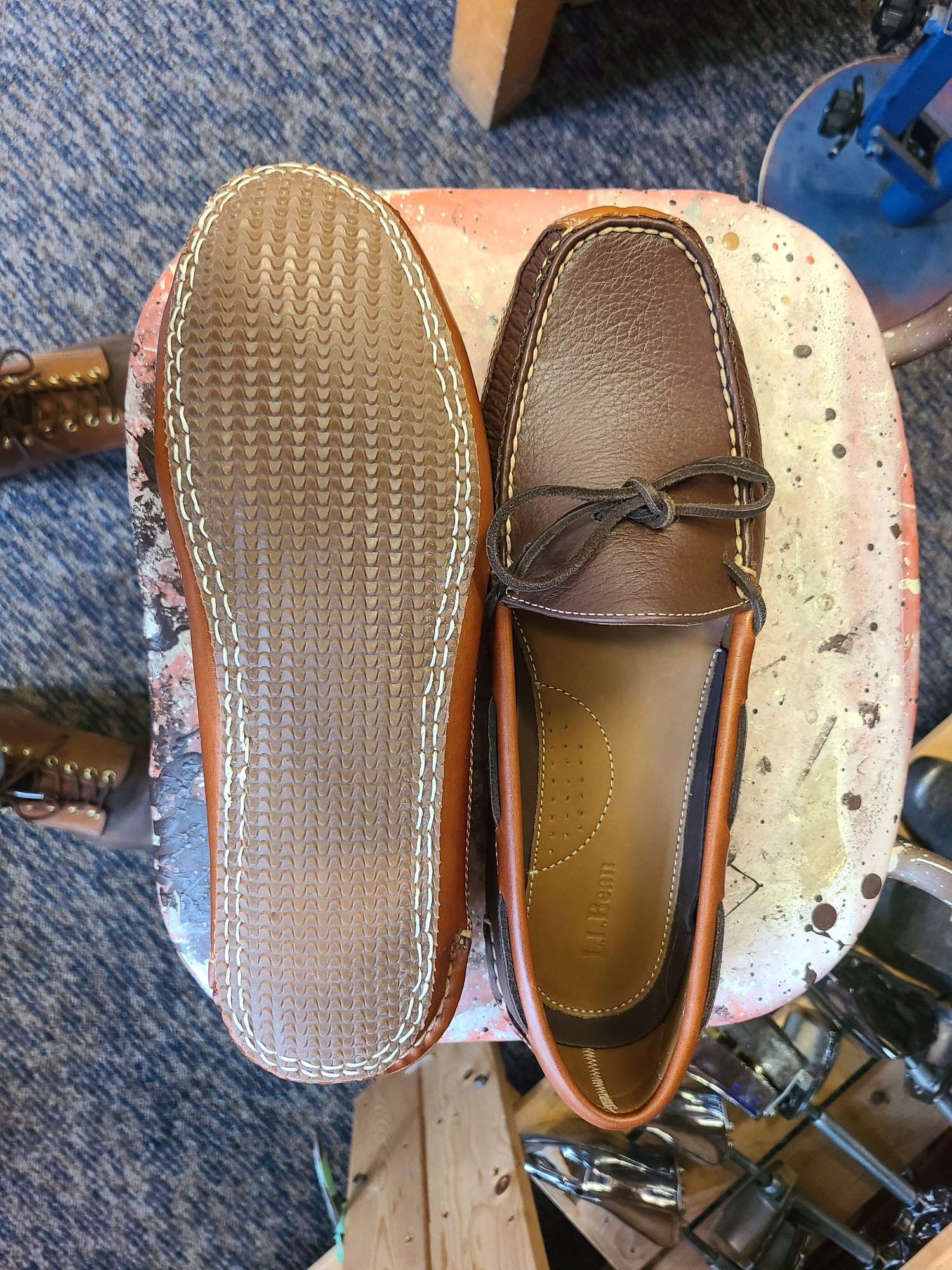 Brown leather shoes with a cap toe design placed on a pink, paint-splattered work surface.